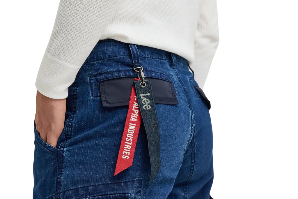 Back side of blue denim alpha industries x lee acu pants showing red and black alpha industries tag on pocket