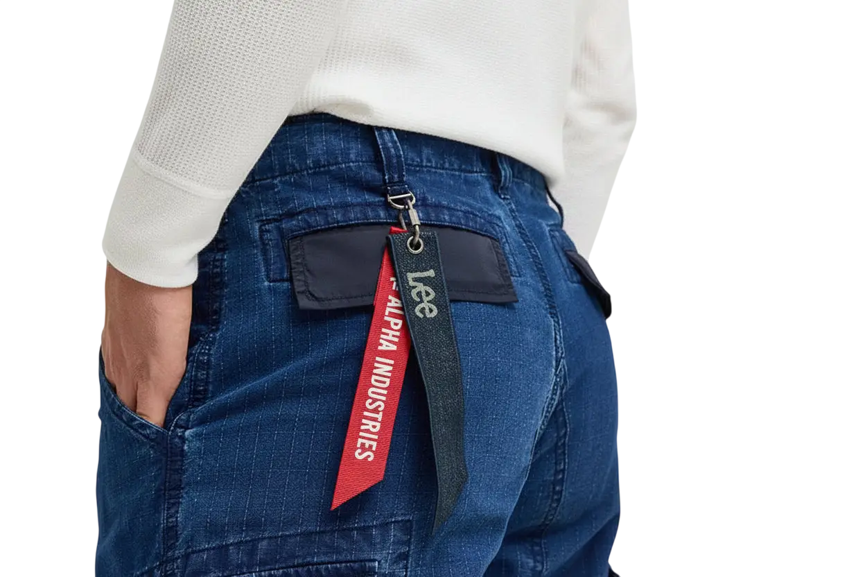 Back side of blue denim alpha industries x lee acu pants showing red and black alpha industries tag on pocket