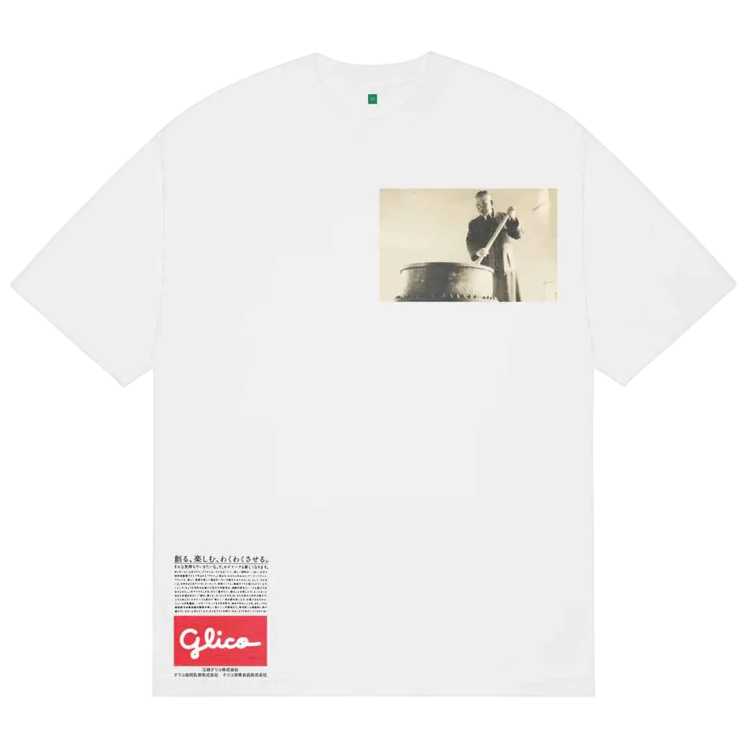 White cotton b.Eautiful Guriko T-shirt featuring a vintage black and white photo of a man playing drum with Glico logo