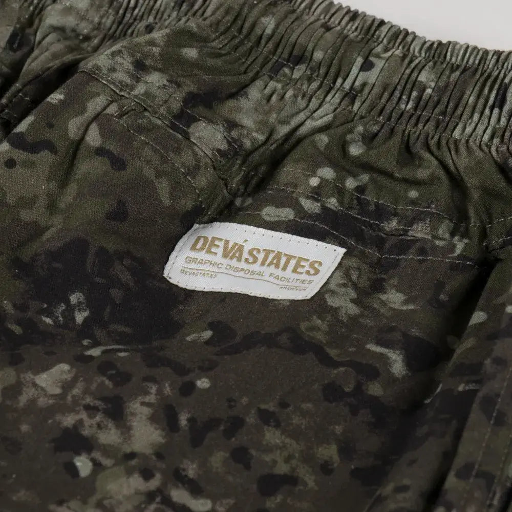Olive green and black camouflage pants with a white devastates label from the deva states camo easy pants collection