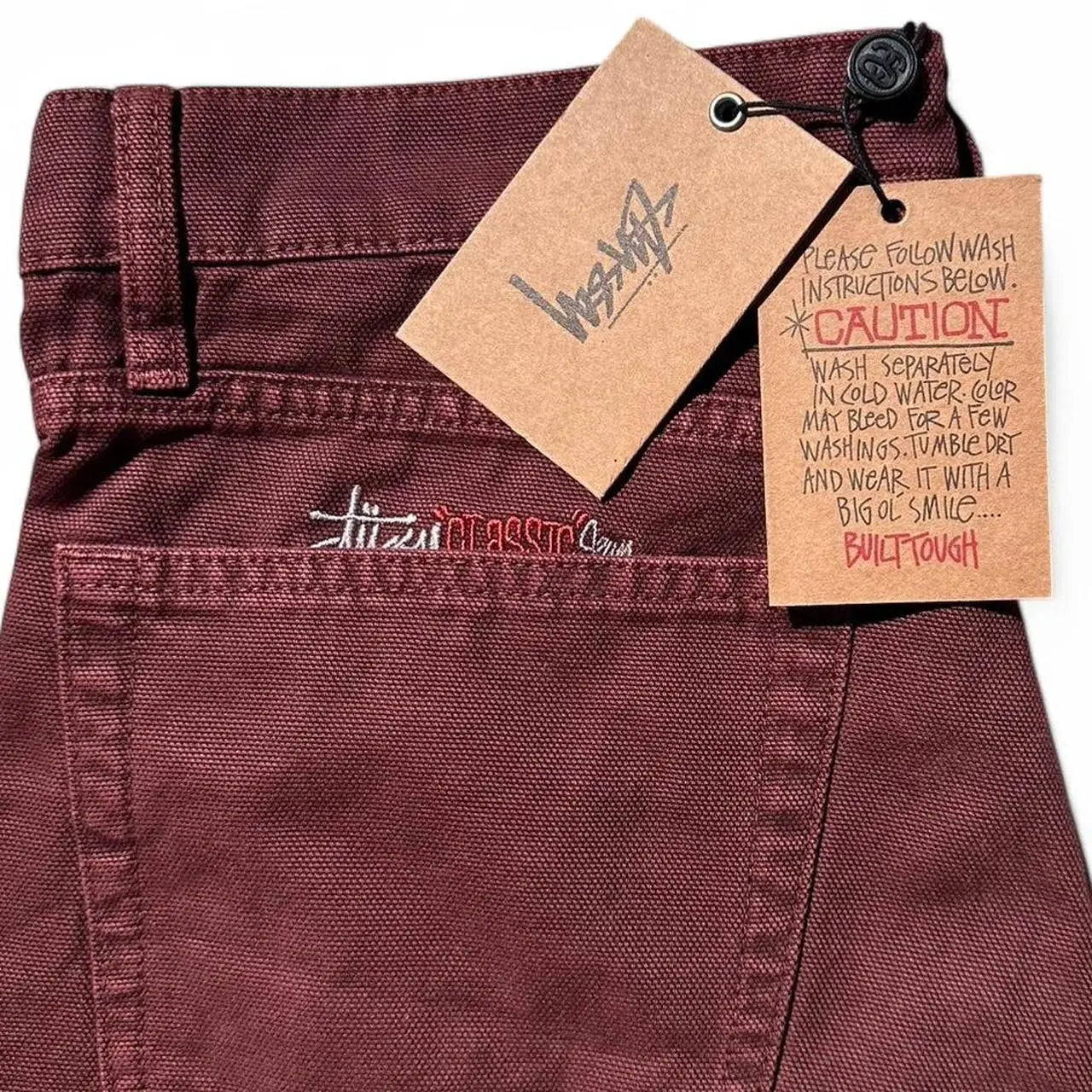 Back side of maroon stussy classic jeans showing washed canvas wine denim with embroidered logo on back pocket