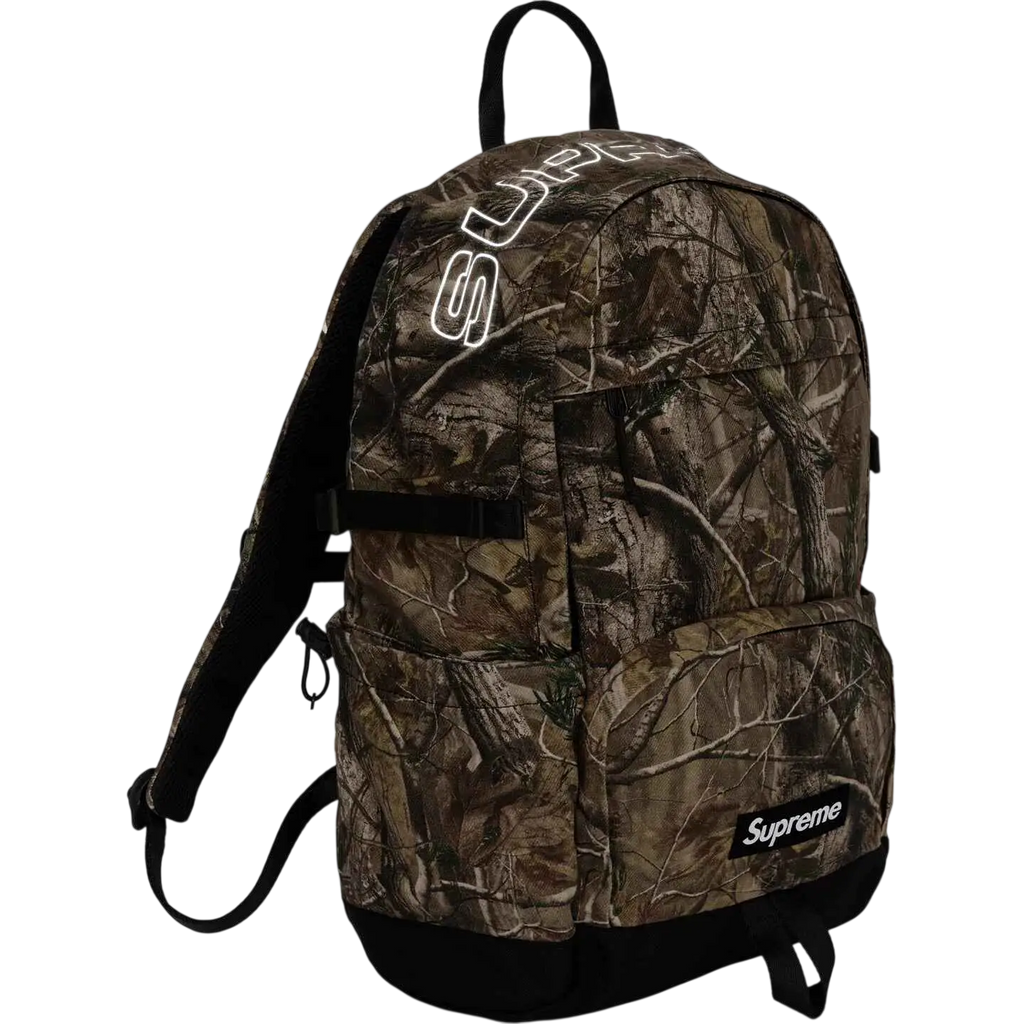 Supreme denim backpack camo fw25 with camouflage pattern, glowing white logo, and black straps visible from the back side