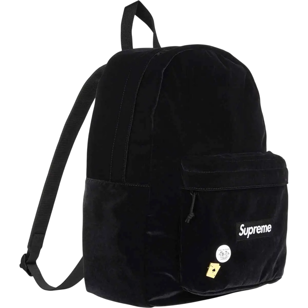 Black velvet Supreme backpack with front pocket featuring brand logo and decorative pins in black color