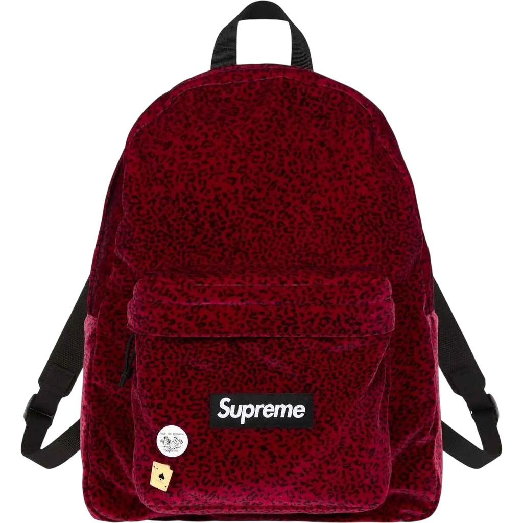 A red velvet supreme backpack with subtle leopard print and decorative pins showcasing the brand logo patch