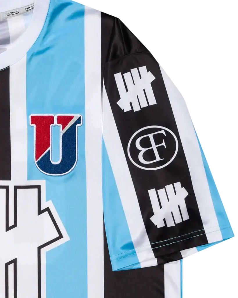Light blue and black striped soccer jersey with red and navy u logo and white lettering on the sleeve by undefeated x badfriend